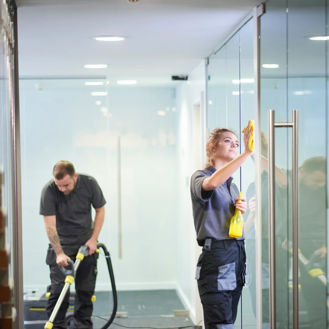 A female employee cleans a glass door while a male employee is seen vacuuming