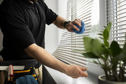 An employee's gloved hands are seen cleaning the some dusty blinds